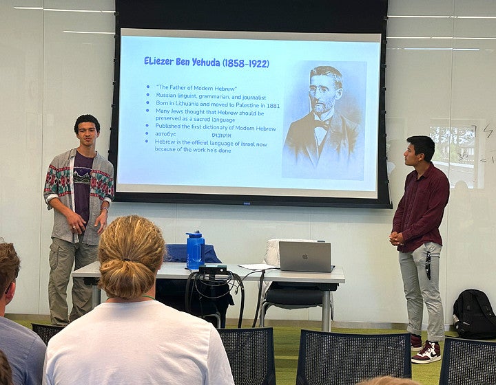 Two students are giving a presentation on stage with a screen behind them