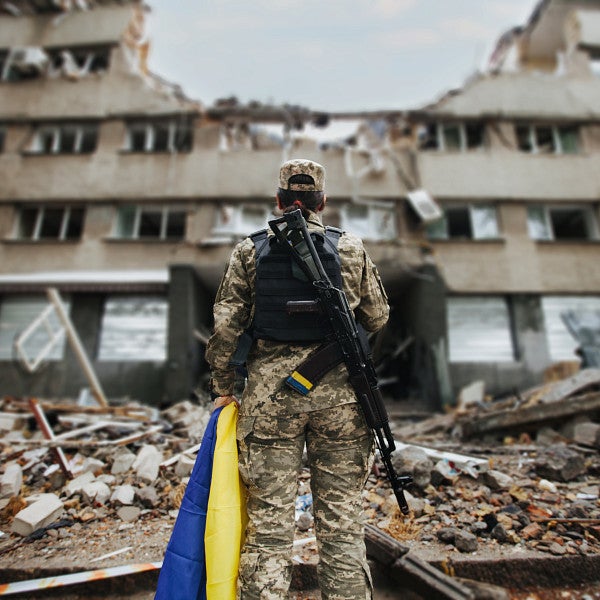 Ukrainian military woman with the Ukrainian flag in her hands on the background of an exploded house